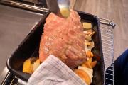Schweinsbraten wird mit Sauce übergossen.