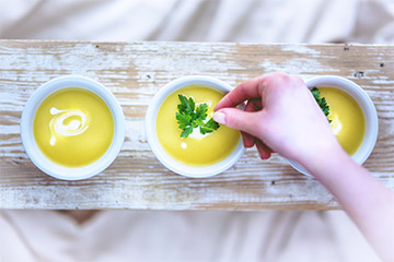 Hand legt Kräuter in eine Suppe.